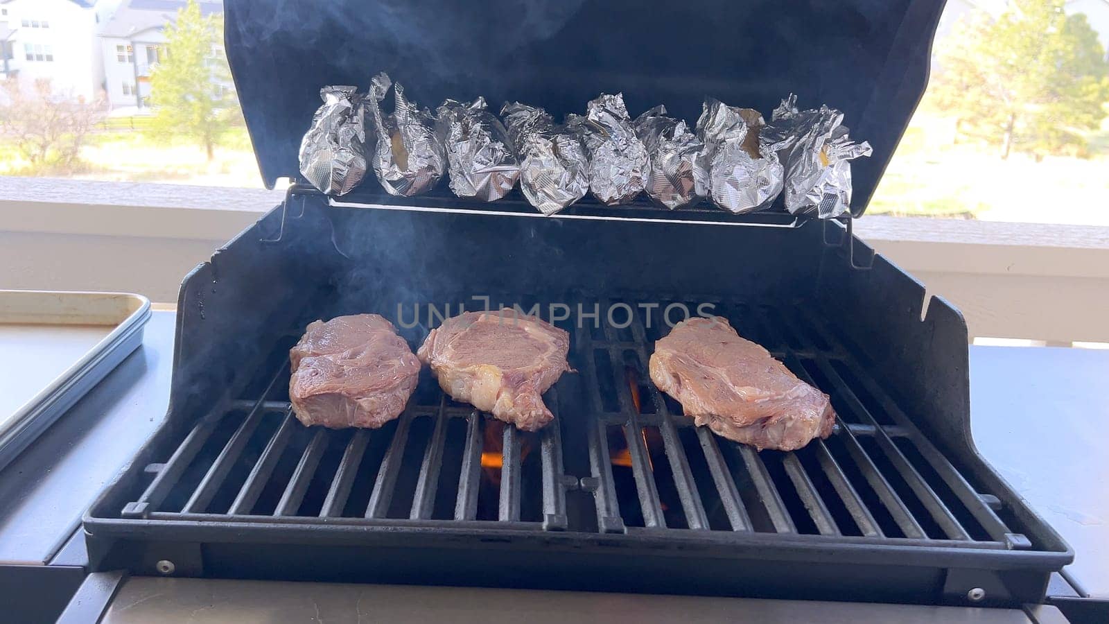 A person uses tongs to flip juicy steaks on a grill, with flames licking the meat, captured in a moment of intense heat and sizzle, showcasing a classic outdoor cooking experience.