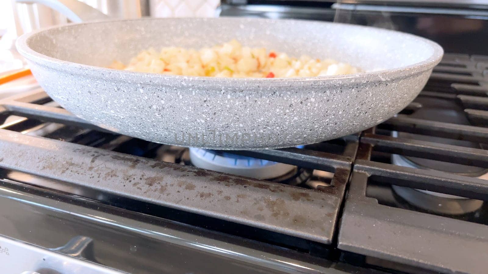 A frying pan on a gas stove sizzles with diced potatoes and colorful bits of red and green peppers, showcasing a delicious and simple home-cooked side dish in the making.