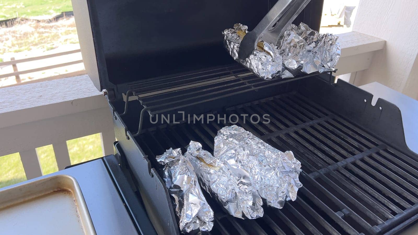 Several ears of corn wrapped in aluminum foil are lined up on a barbecue grill, slowly roasting to perfection, showcasing a popular and delicious method of cooking this classic side dish.