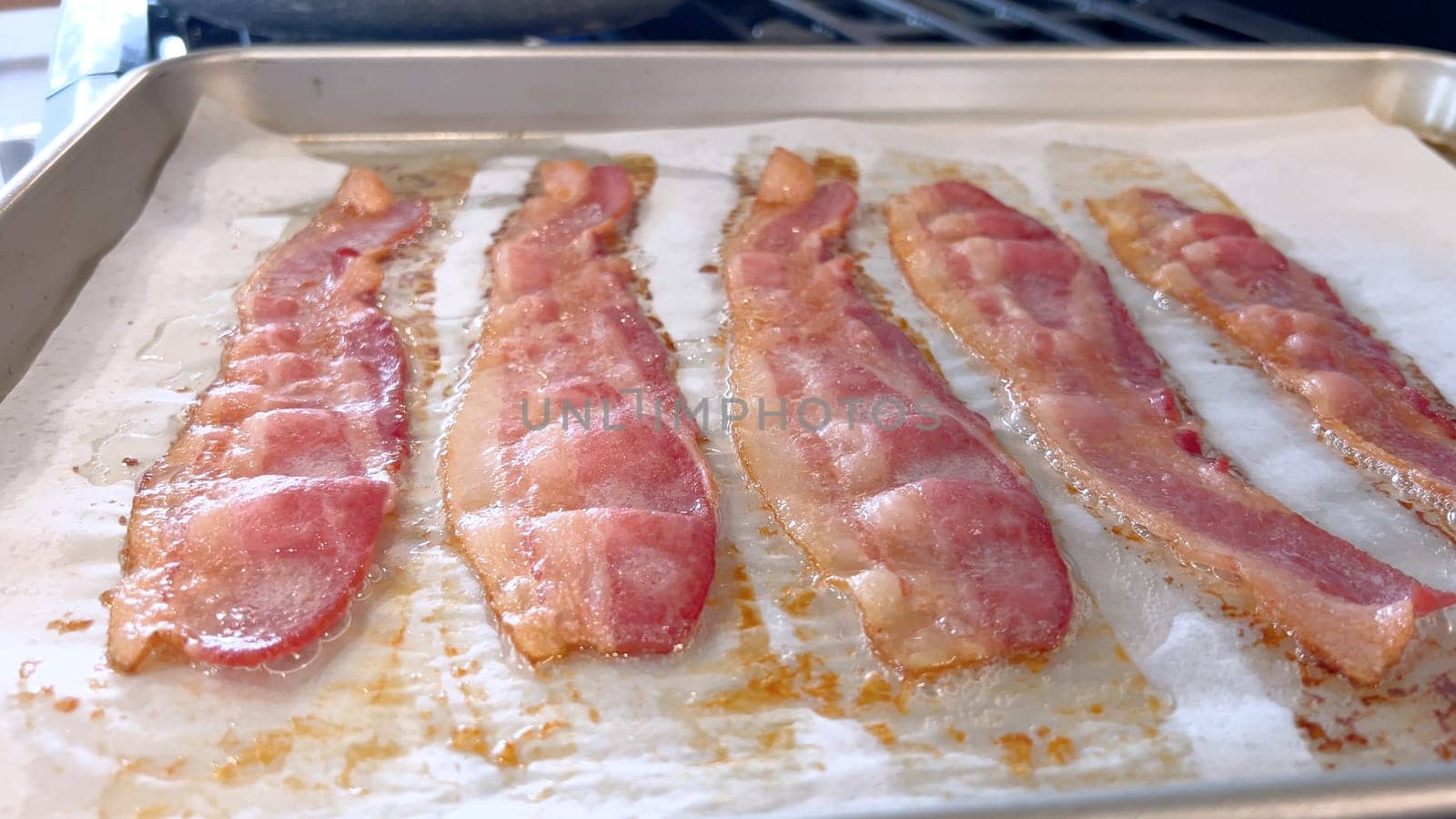Sizzling Bacon Strips Baking on a Parchment-Lined Tray by arinahabich