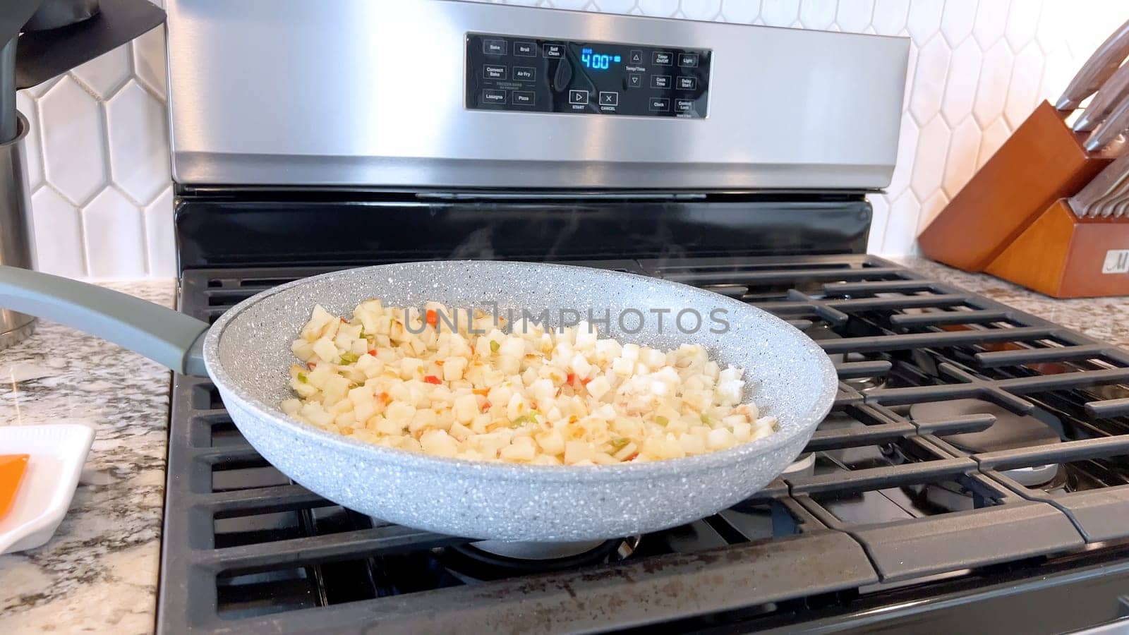 A frying pan on a gas stove sizzles with diced potatoes and colorful bits of red and green peppers, showcasing a delicious and simple home-cooked side dish in the making.