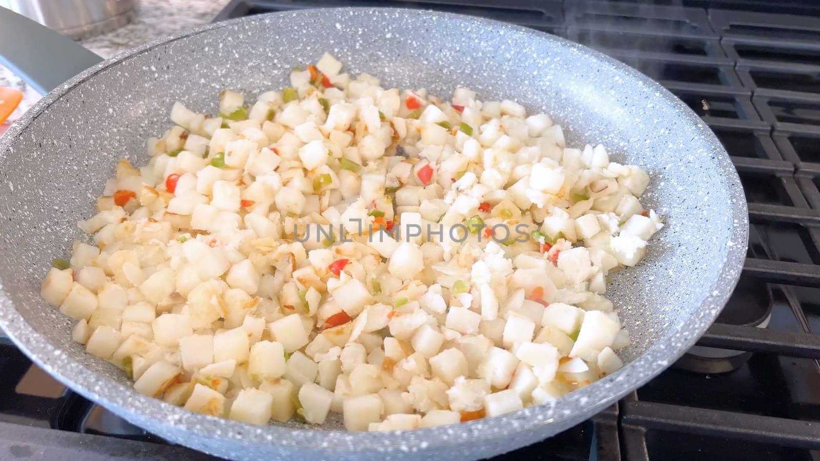 A frying pan on a gas stove sizzles with diced potatoes and colorful bits of red and green peppers, showcasing a delicious and simple home-cooked side dish in the making.