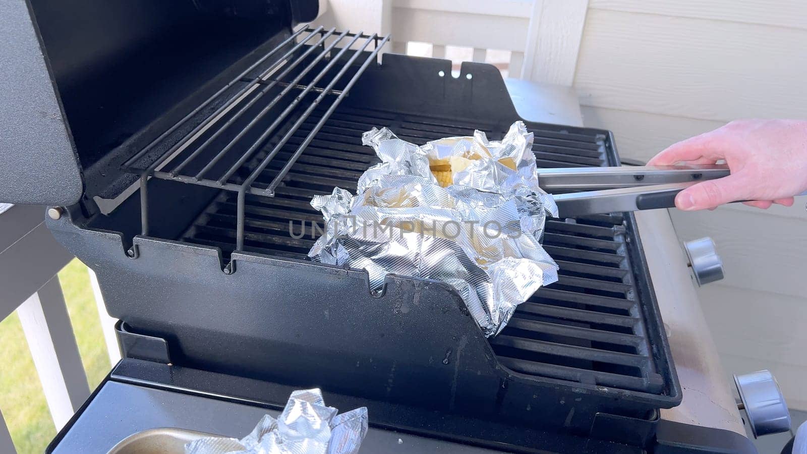 Several ears of corn wrapped in aluminum foil are lined up on a barbecue grill, slowly roasting to perfection, showcasing a popular and delicious method of cooking this classic side dish.