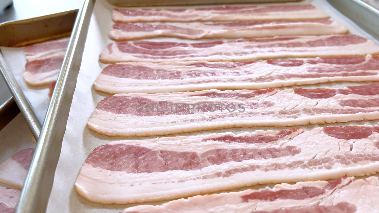 Neatly arranged raw bacon strips on a baking tray, prepared for cooking, capturing the fresh, uncooked look of this popular breakfast ingredient before it turns crispy and golden.