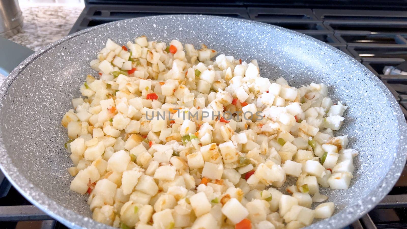 A frying pan on a gas stove sizzles with diced potatoes and colorful bits of red and green peppers, showcasing a delicious and simple home-cooked side dish in the making.