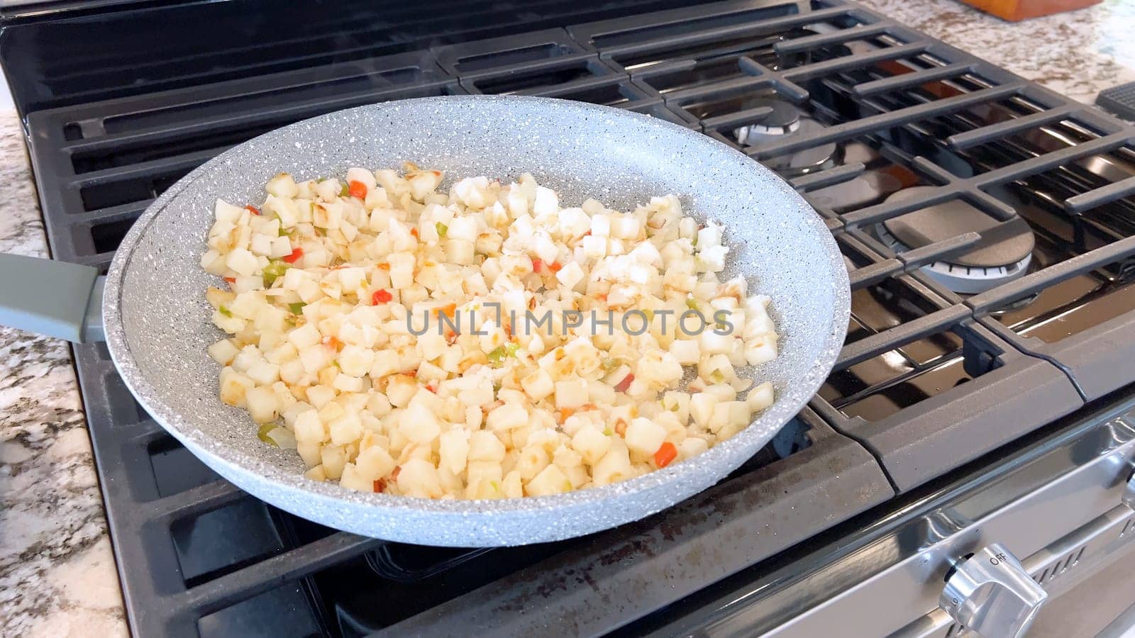 A frying pan on a gas stove sizzles with diced potatoes and colorful bits of red and green peppers, showcasing a delicious and simple home-cooked side dish in the making.