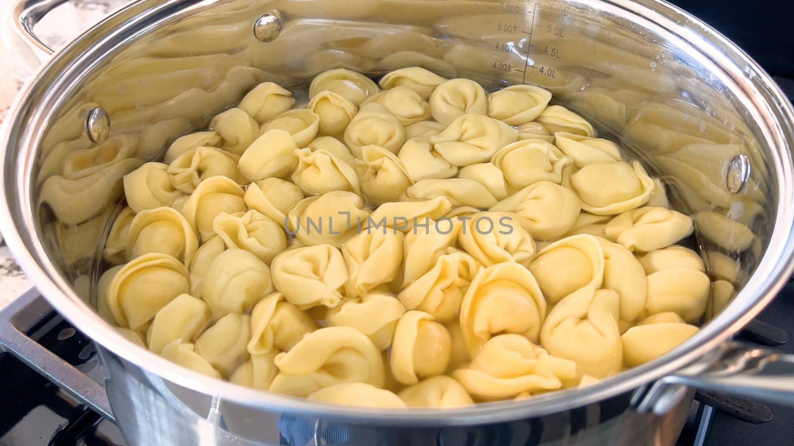 A large pot filled with boiling tortellini pasta showcases the preparation of this traditional Italian dish, with the pasta floating in water ready to be served, set on a modern gas stove.