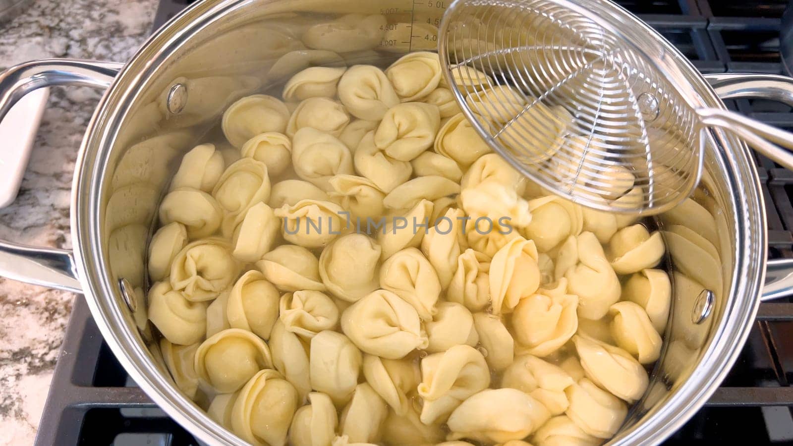 A large pot filled with boiling tortellini pasta showcases the preparation of this traditional Italian dish, with the pasta floating in water ready to be served, set on a modern gas stove.