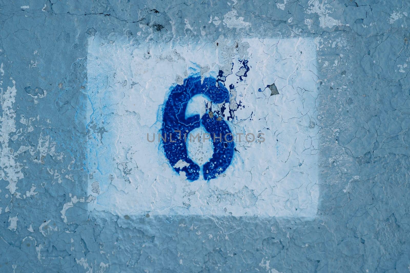 Number six painted on a blue scratched wall in a rectangle with peeling paint by Nadtochiy