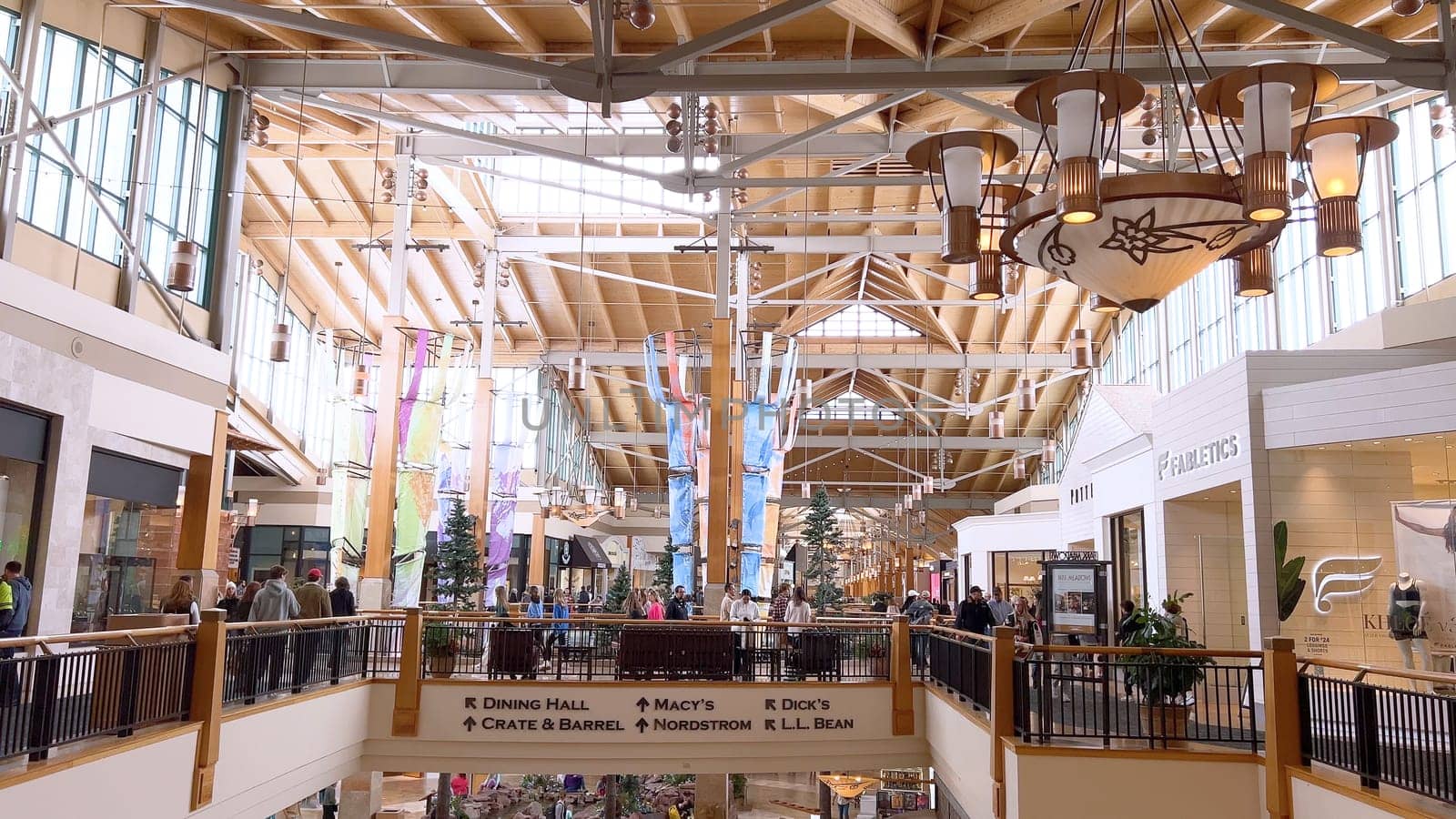 Denver, Colorado, USA-April 28, 2024- Capturing the expansive and airy interior of Park Meadows Mall, this image highlights the modern architectural style with wooden beams, large hanging lights, and a series of vibrant hanging ribbons, creating a lively shopping atmosphere.