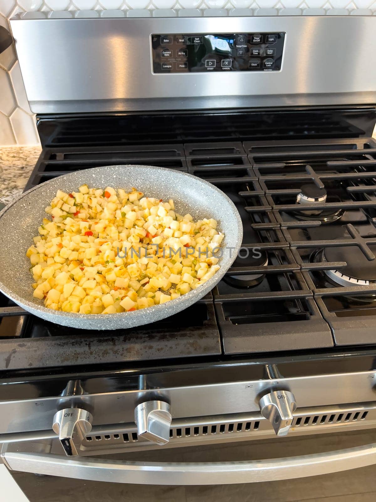 A frying pan on a gas stove sizzles with diced potatoes and colorful bits of red and green peppers, showcasing a delicious and simple home-cooked side dish in the making.