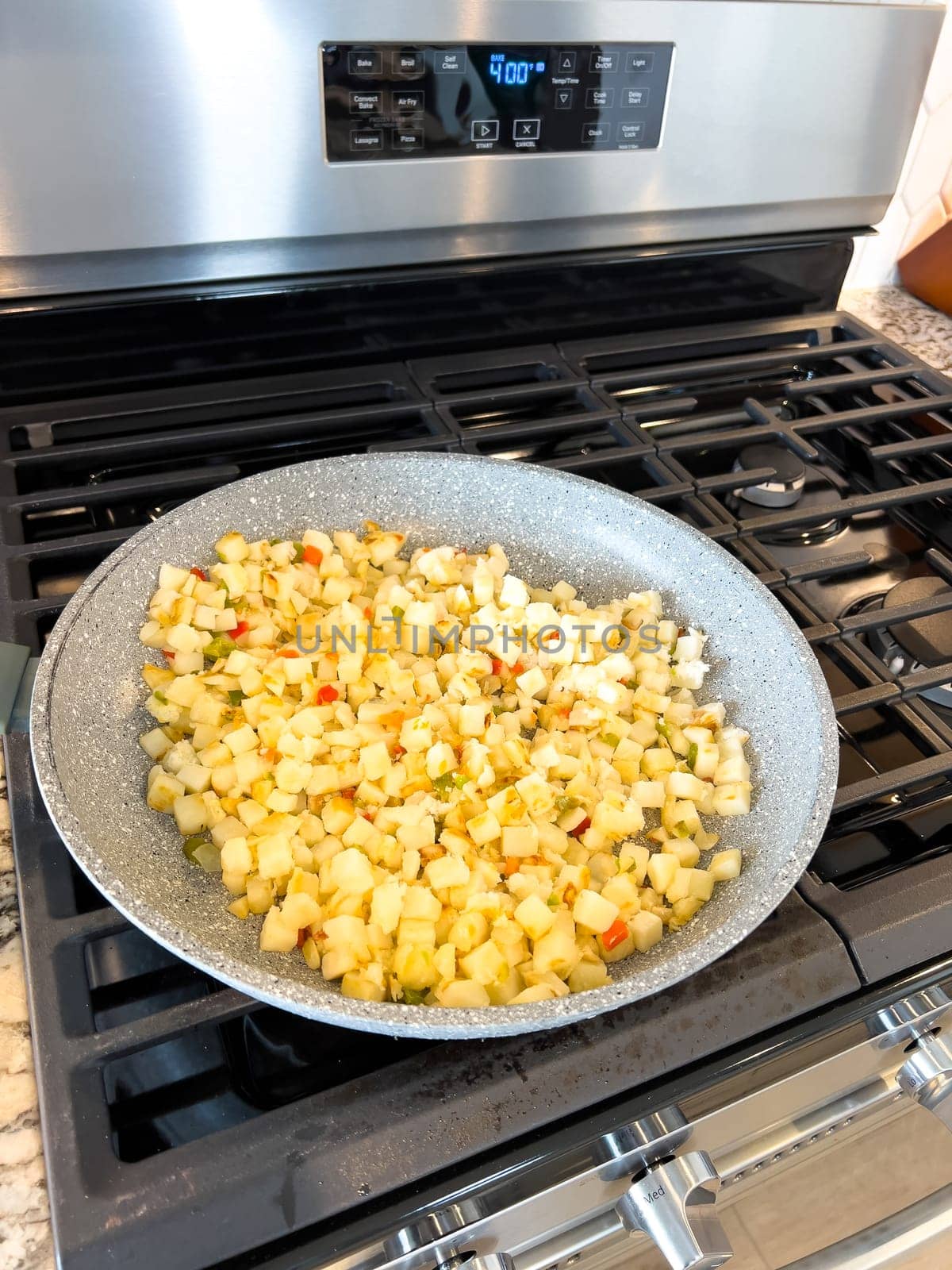 A frying pan on a gas stove sizzles with diced potatoes and colorful bits of red and green peppers, showcasing a delicious and simple home-cooked side dish in the making.