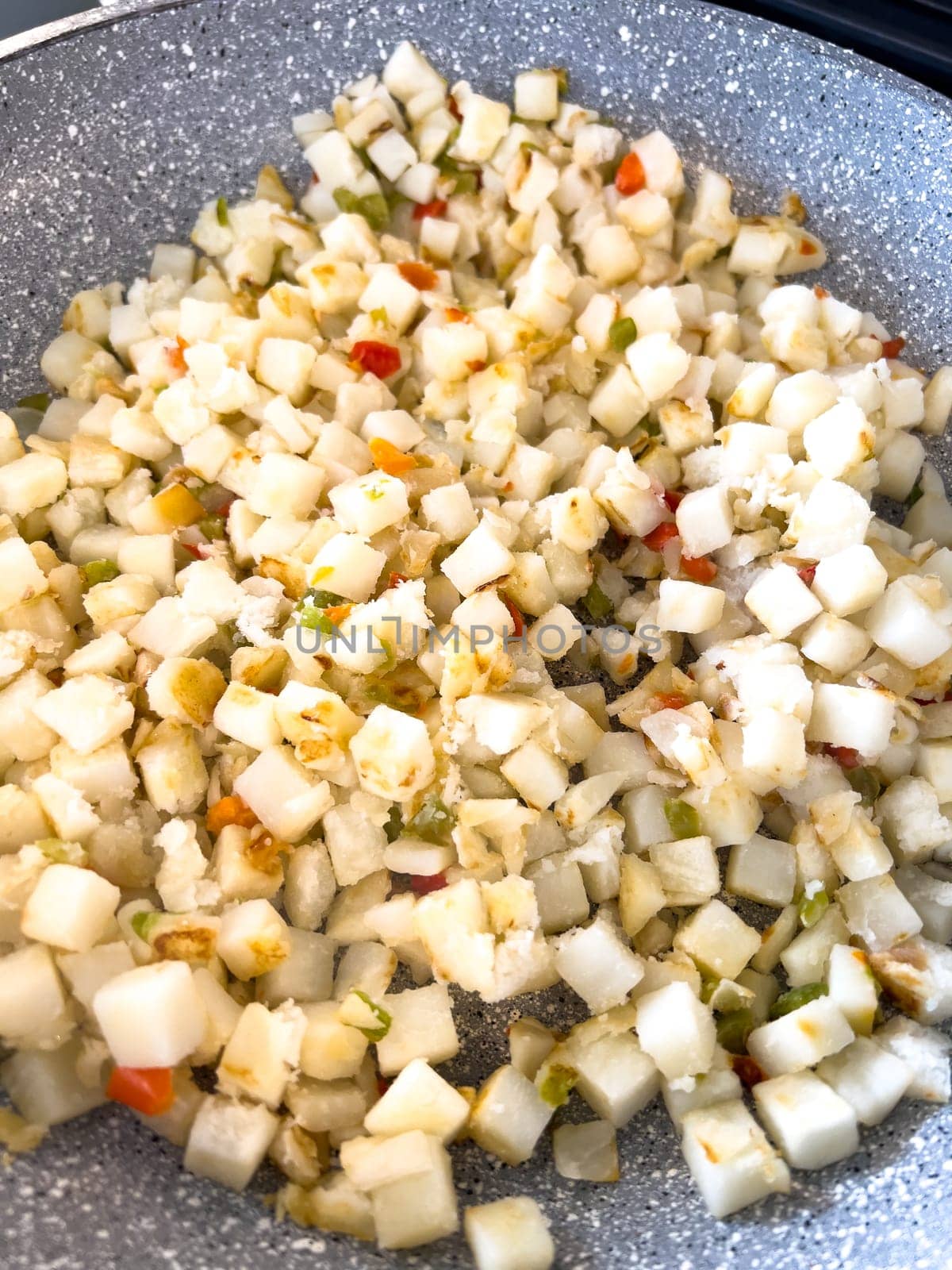 A frying pan on a gas stove sizzles with diced potatoes and colorful bits of red and green peppers, showcasing a delicious and simple home-cooked side dish in the making.