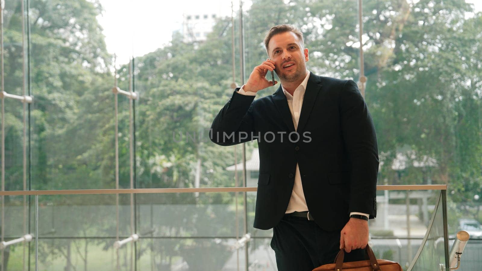 Caucasian businessman calling manager by using smart phone and discuss about financial report. Male leader talking marketing team by using telephone while standing at stair in modern building. Urbane.