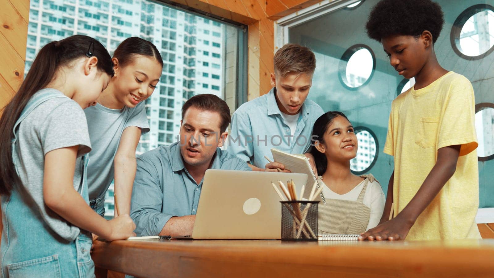 Caucasian teacher giving comment or advise student while smart bot pointing at laptop screen at classroom. Diverse student taking a note while teacher teach lesson while using computer. Edification.