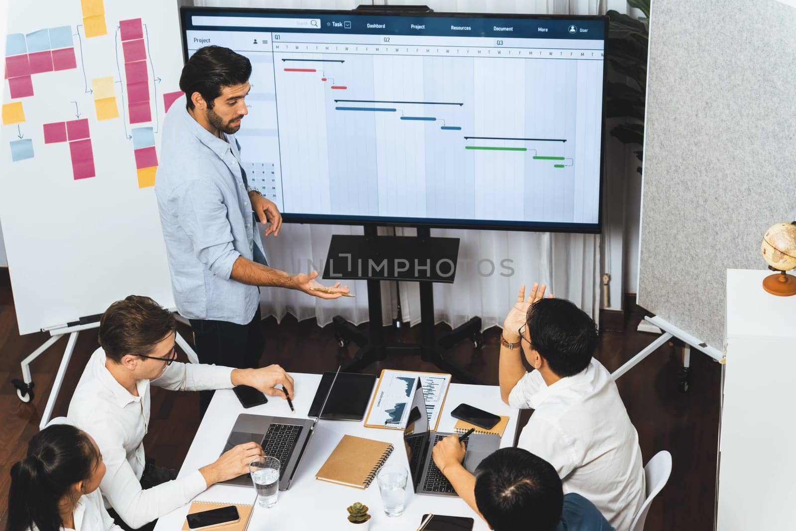 Project manager communicate and collaborate with team using project management software display on monitor, tracking progress of project task and making schedule plan at meeting table. Prudent