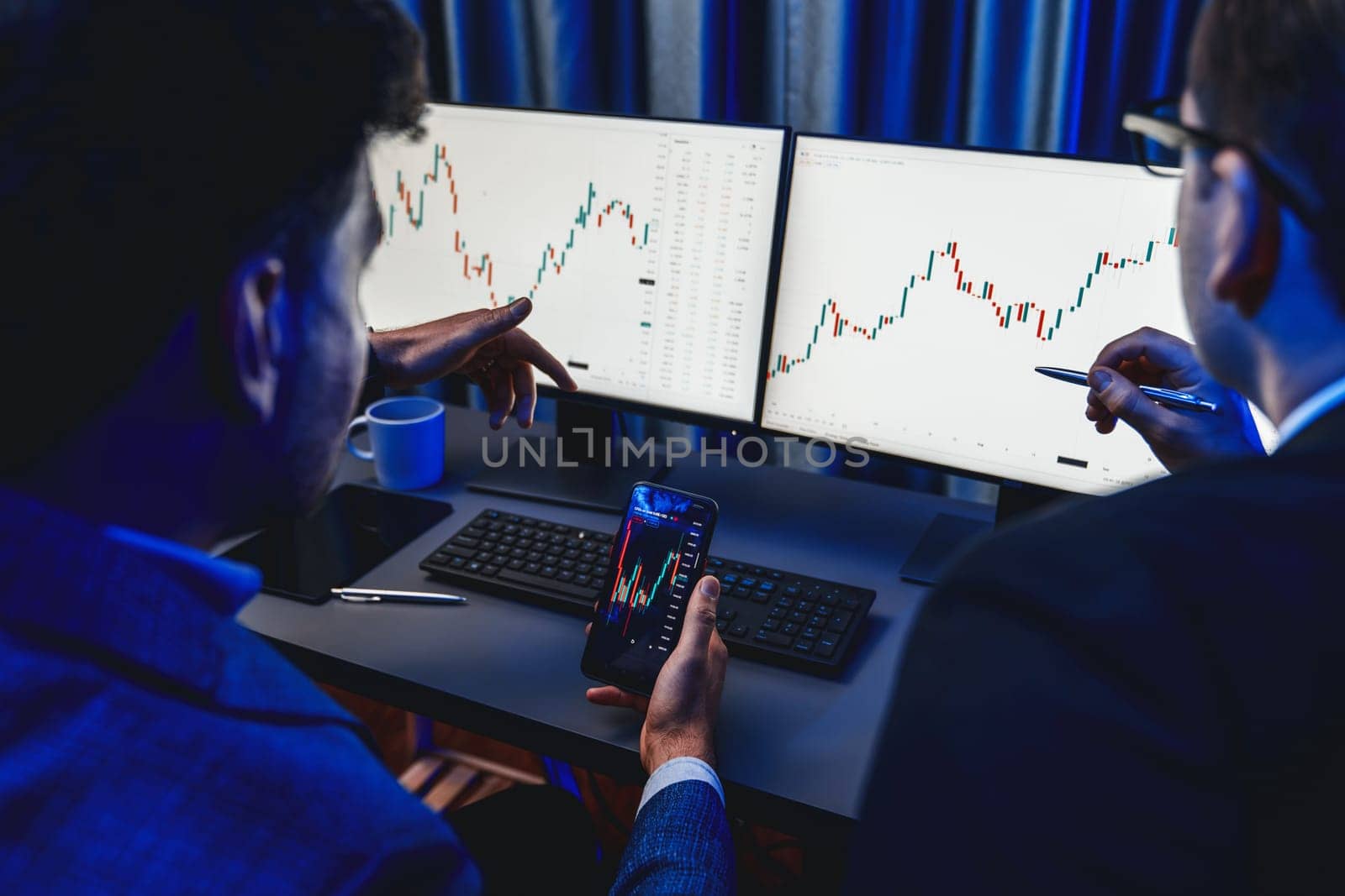 Two stock exchange traders researching data on smartphone and laptop screen server of dynamic digital currency. Investors analyzing market stock at decorative neon blue-light of workplace. Sellable.