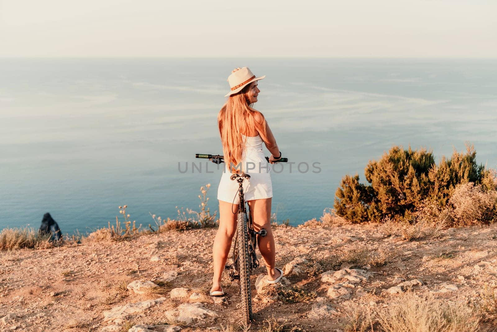 A woman cyclist on a mountain bike looking at the landscape sea. Adventure travel on bike. by Matiunina