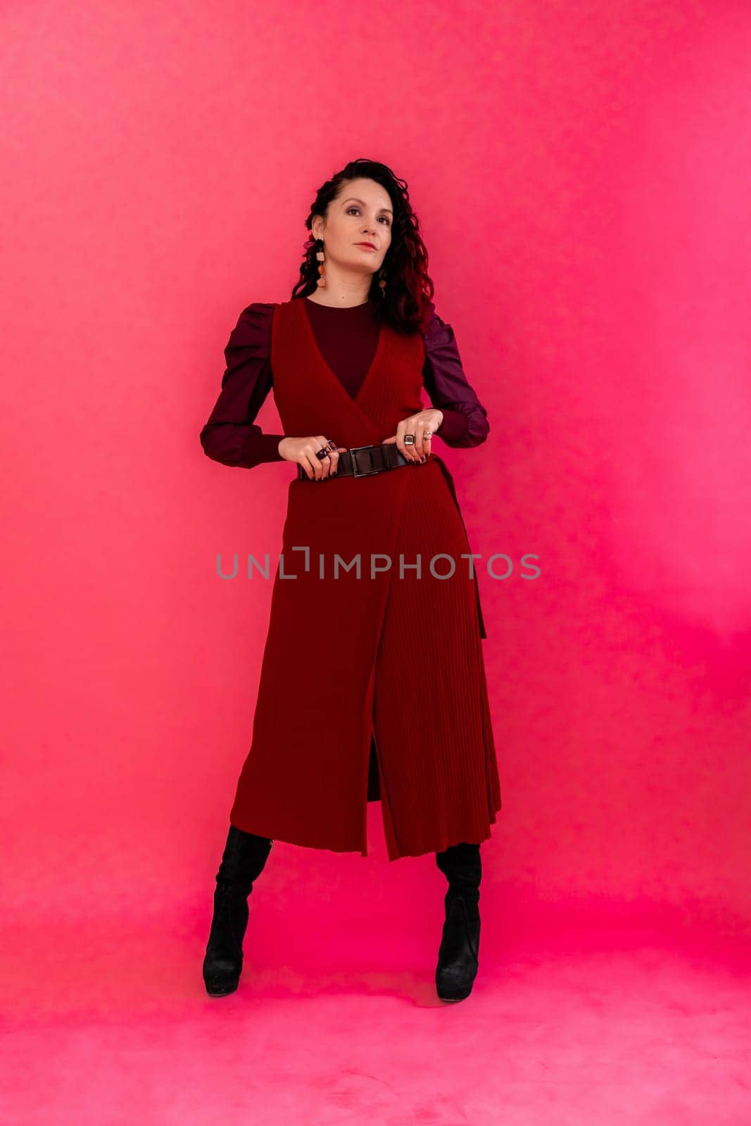 A woman in a red dress poses for the camera. She is wearing black boots and a belt. by Matiunina