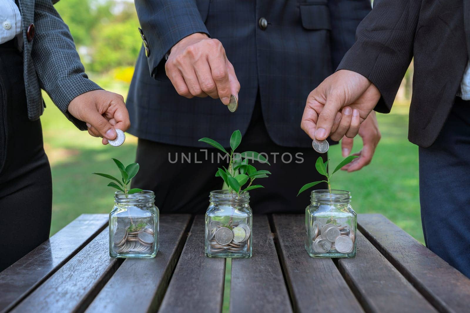 Business people put coin to money saving glass jar on outdoor table as sustainable money growth investment or eco-subsidize. Green corporate promot and invest in environmental awareness. Gyre