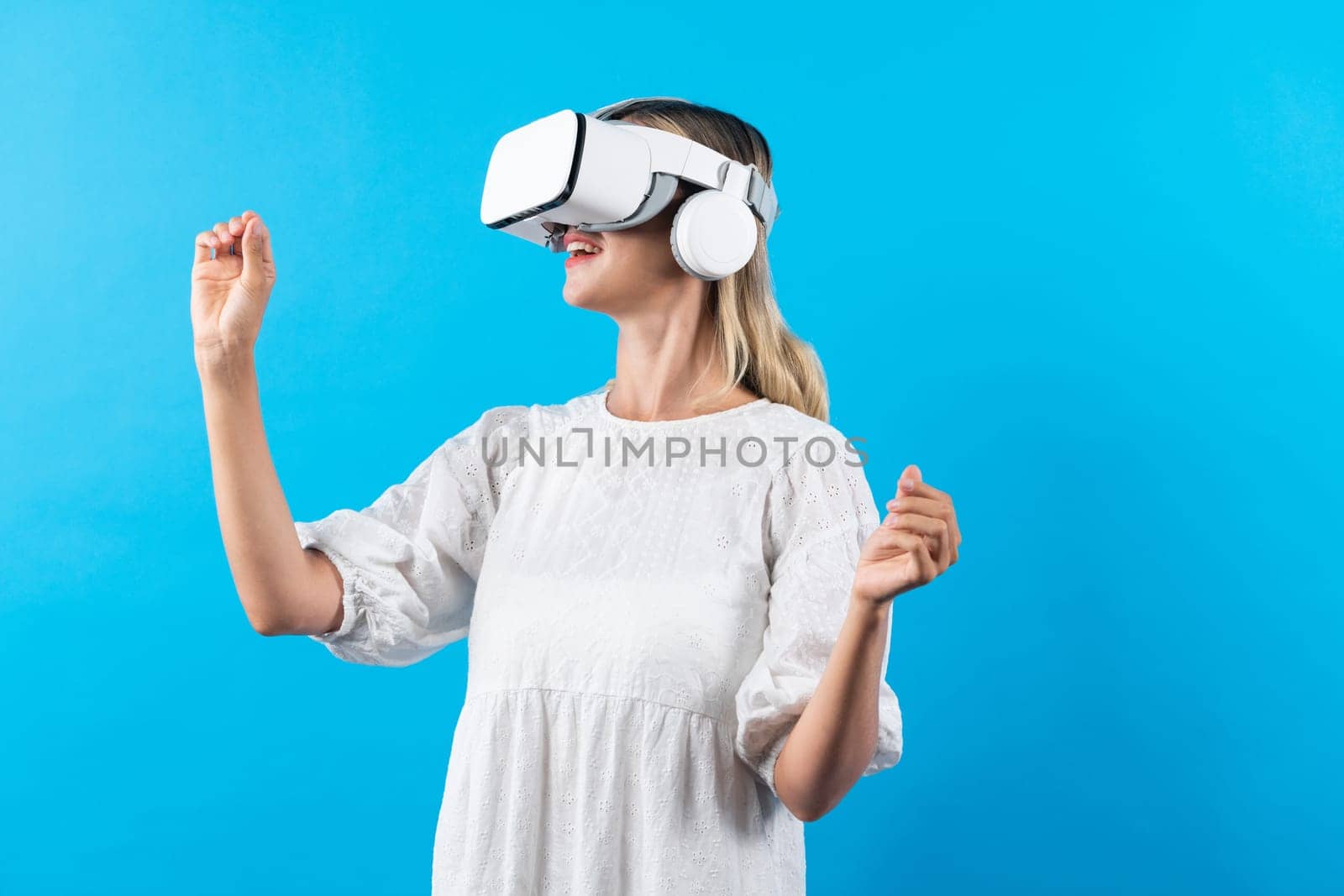 Girl smells flower while wearing VR glasses at blue background. Happy woman with VR goggle enjoy looking nature hologram while connection with visual reality world. Technology innovation. Contraption.