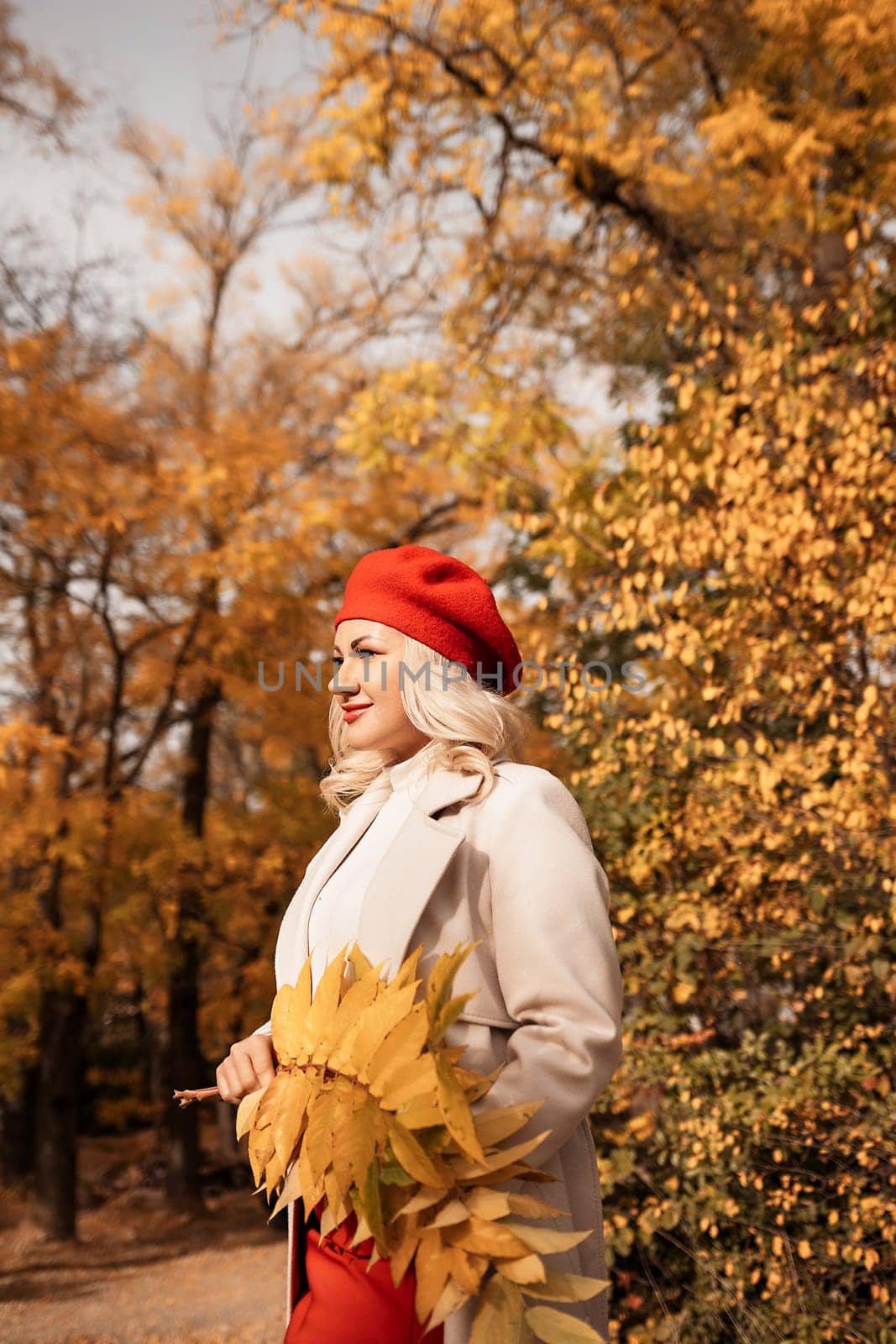 autumn woman in a red beret, a light coat and a red skirt, against the backdrop of an autumn park with yellow leaves in her hands by Matiunina