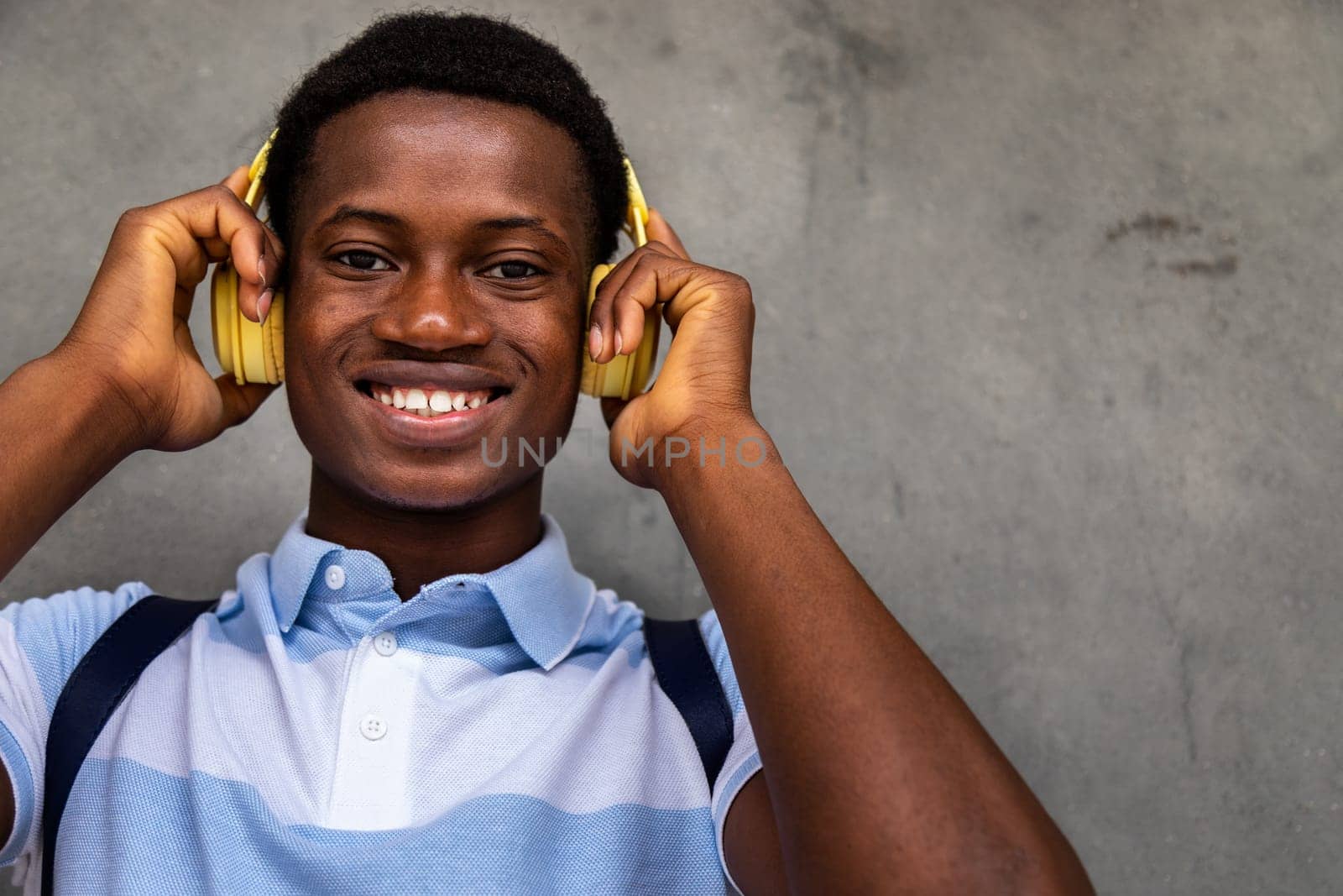 Happy teen African American boy looking at camera wearing headphones. Copy space. by Hoverstock