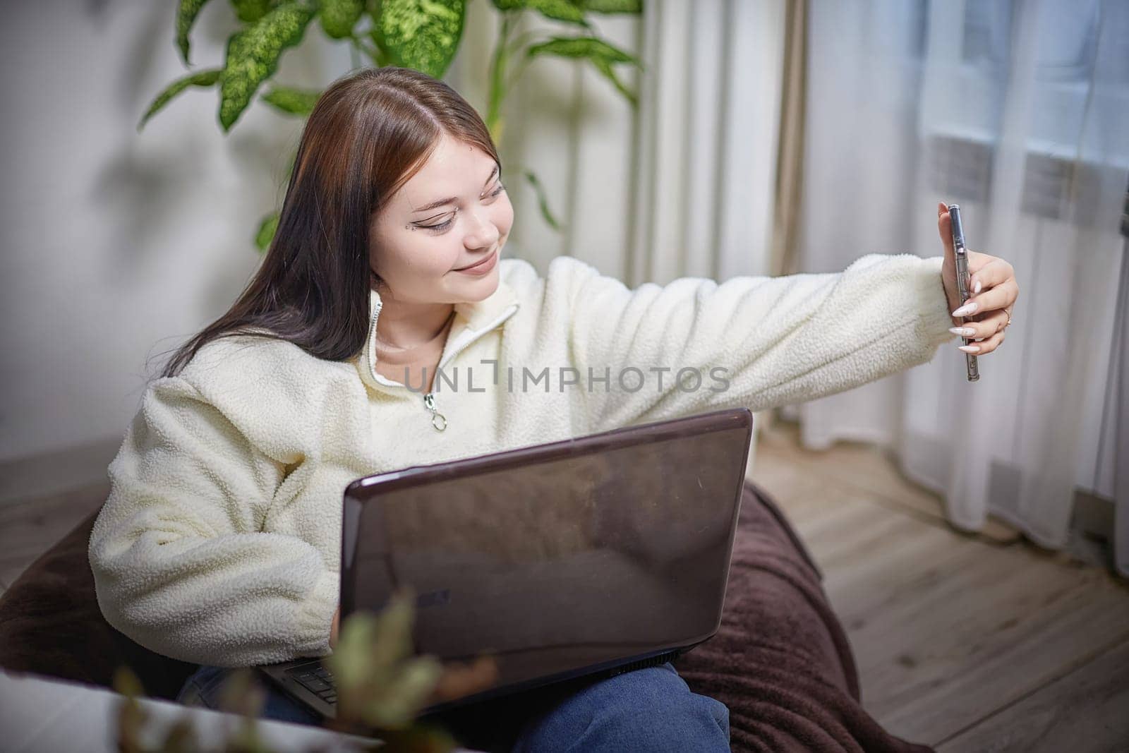 Modern Stylish chubby student brunette girl taking selfie with cell mobile phone. Picture of attractive young brunette overweight indoors by keleny