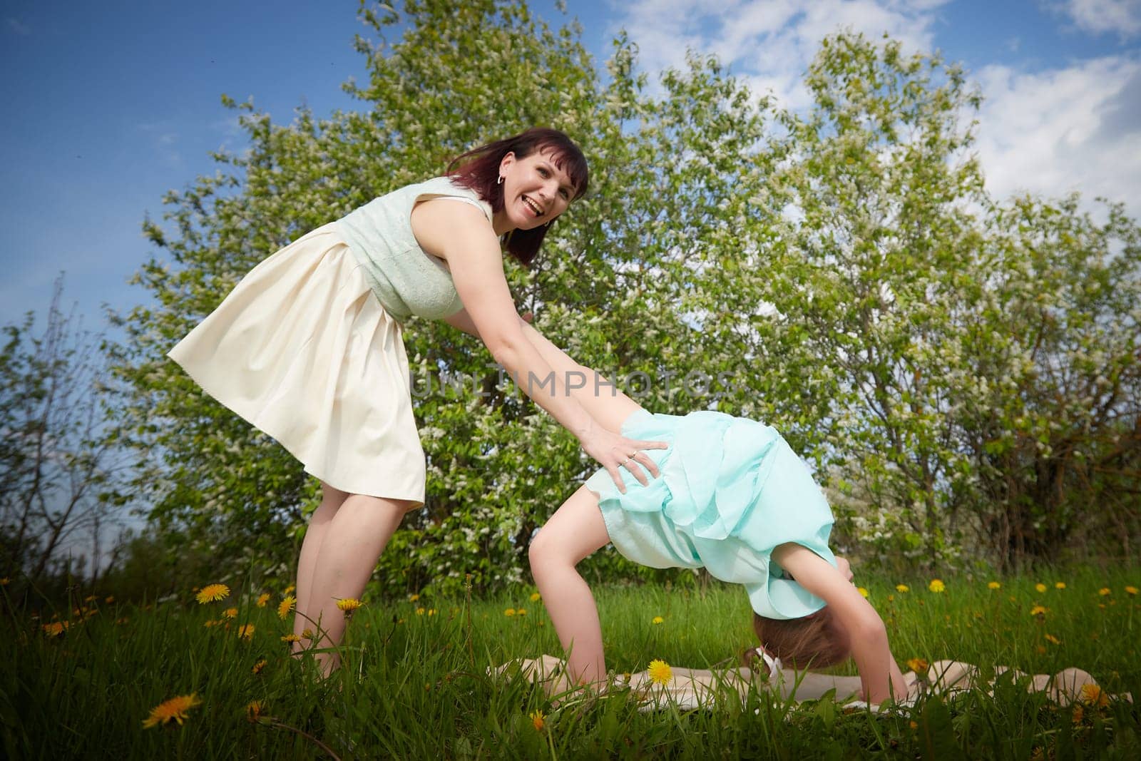 Happy mother and daughter enjoying rest, playing, fun and doing sports exercises on nature in a green field. Woman and girl resting outdoors in summer and spring day