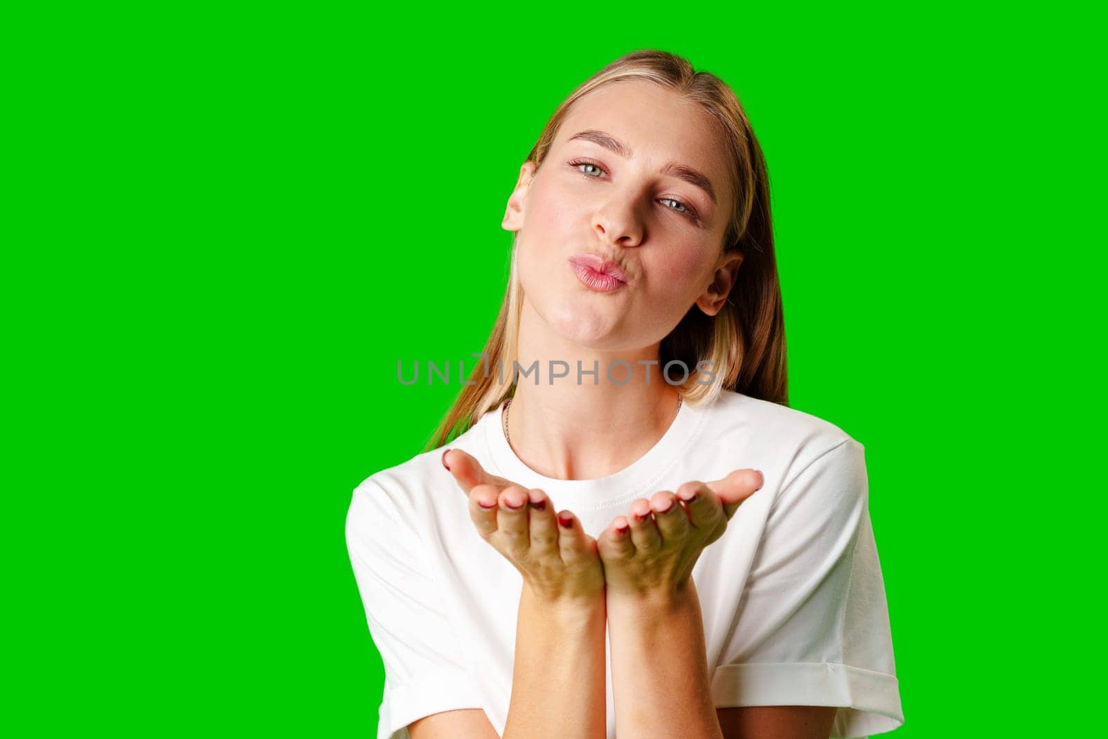 Young Woman Blowing a Kiss With a Playful Expression Against a Bright Green Background in studio