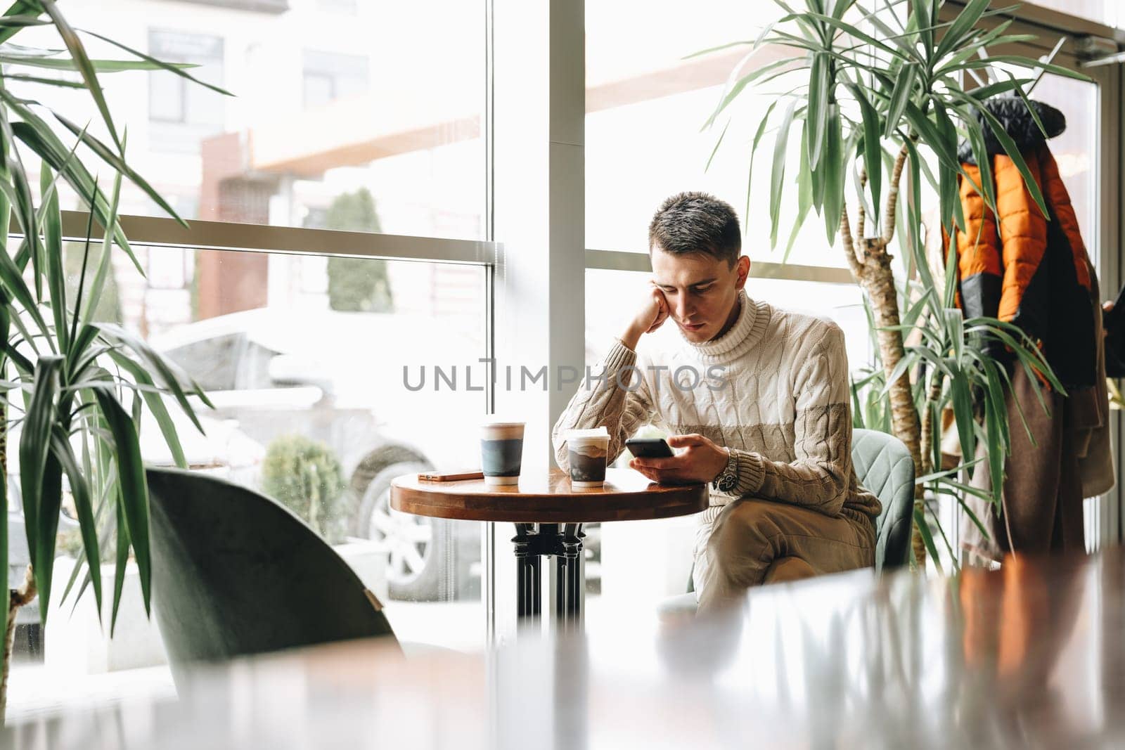 Young Man Engrossed in Smartphone at a Modern Cafe During Daytime by Fabrikasimf