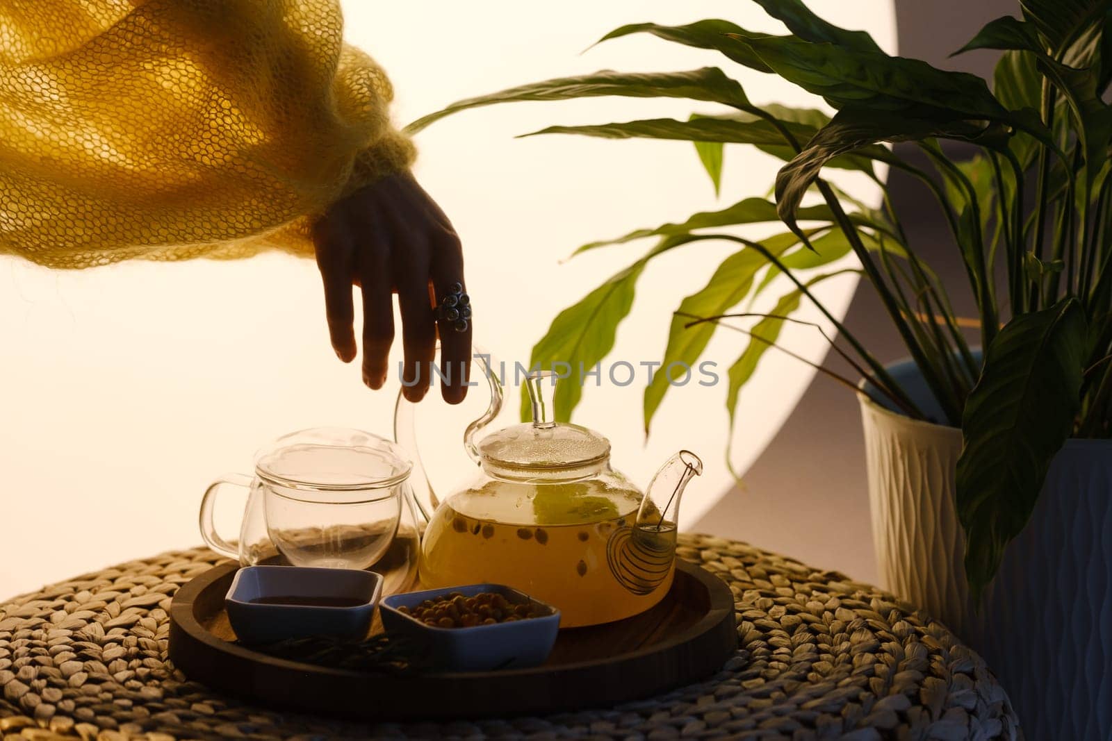 Close-up of a hand with a kettle. A teapot with sea buckthorn tea, honey and a plate with sea buckthorn on a tray.