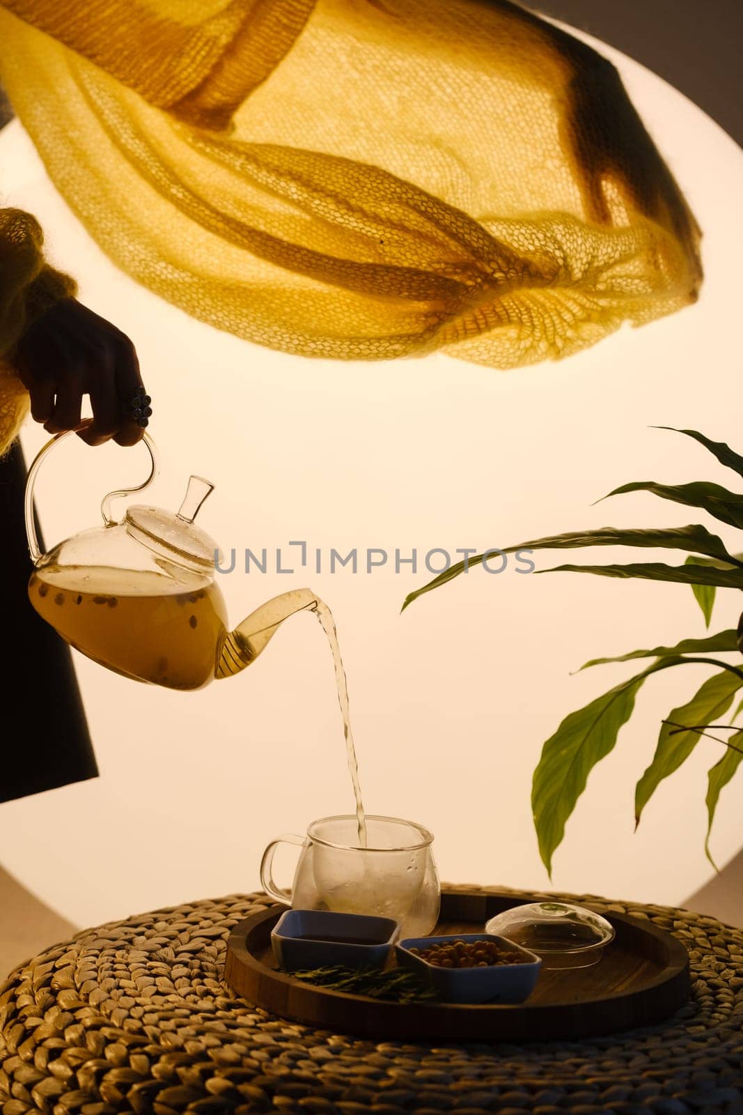 Close-up of a hand with a kettle. A teapot with sea buckthorn tea, honey and a plate with sea buckthorn on a tray by Lobachad