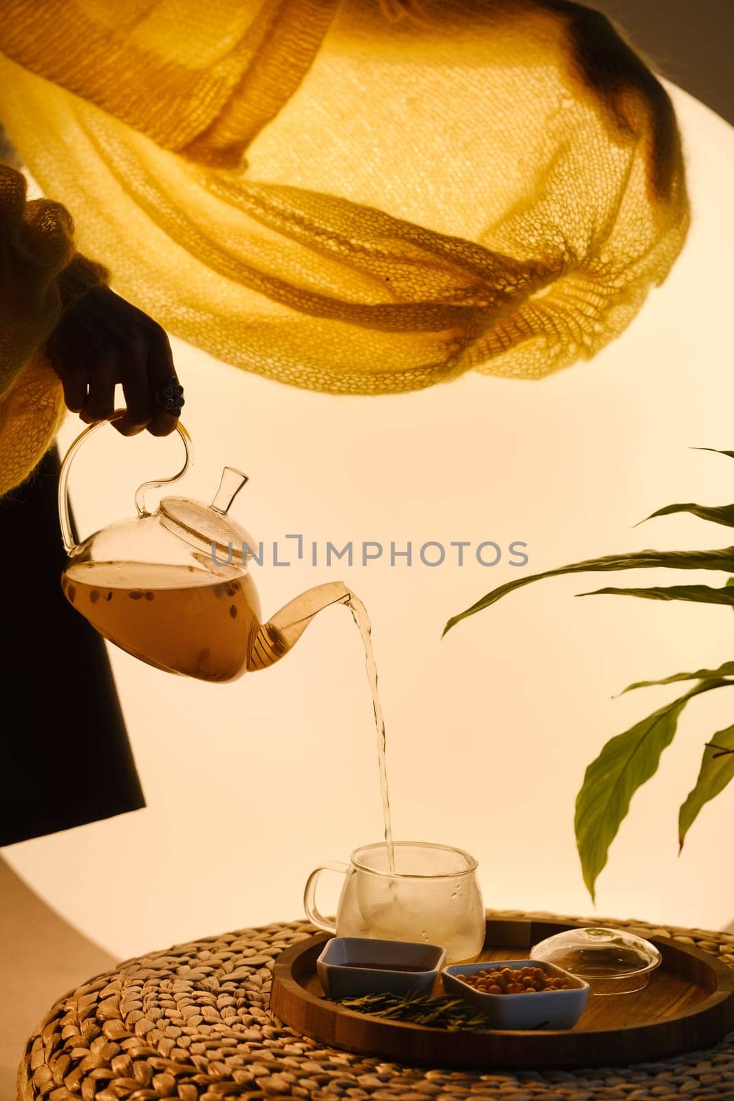 Close-up of a hand with a kettle. A teapot with sea buckthorn tea, honey and a plate with sea buckthorn on a tray by Lobachad