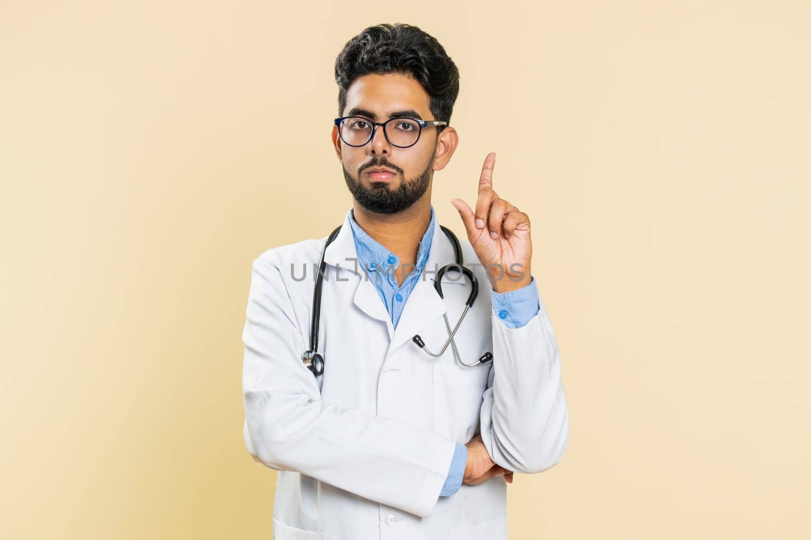 Displeased upset Indian young doctor cardiologist man reacting to unpleasant awful idea, dissatisfied with bad work, wave hand, shake head No dismiss bad idea proposal. Arabian guy on beige background