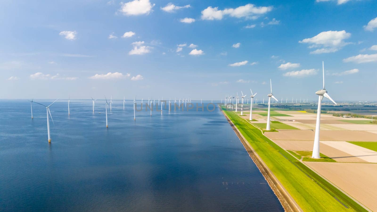 A mesmerizing overhead view captures the graceful dance of windmill turbines in a vast oceanic wind farm, located in the Netherlands Flevoland by fokkebok