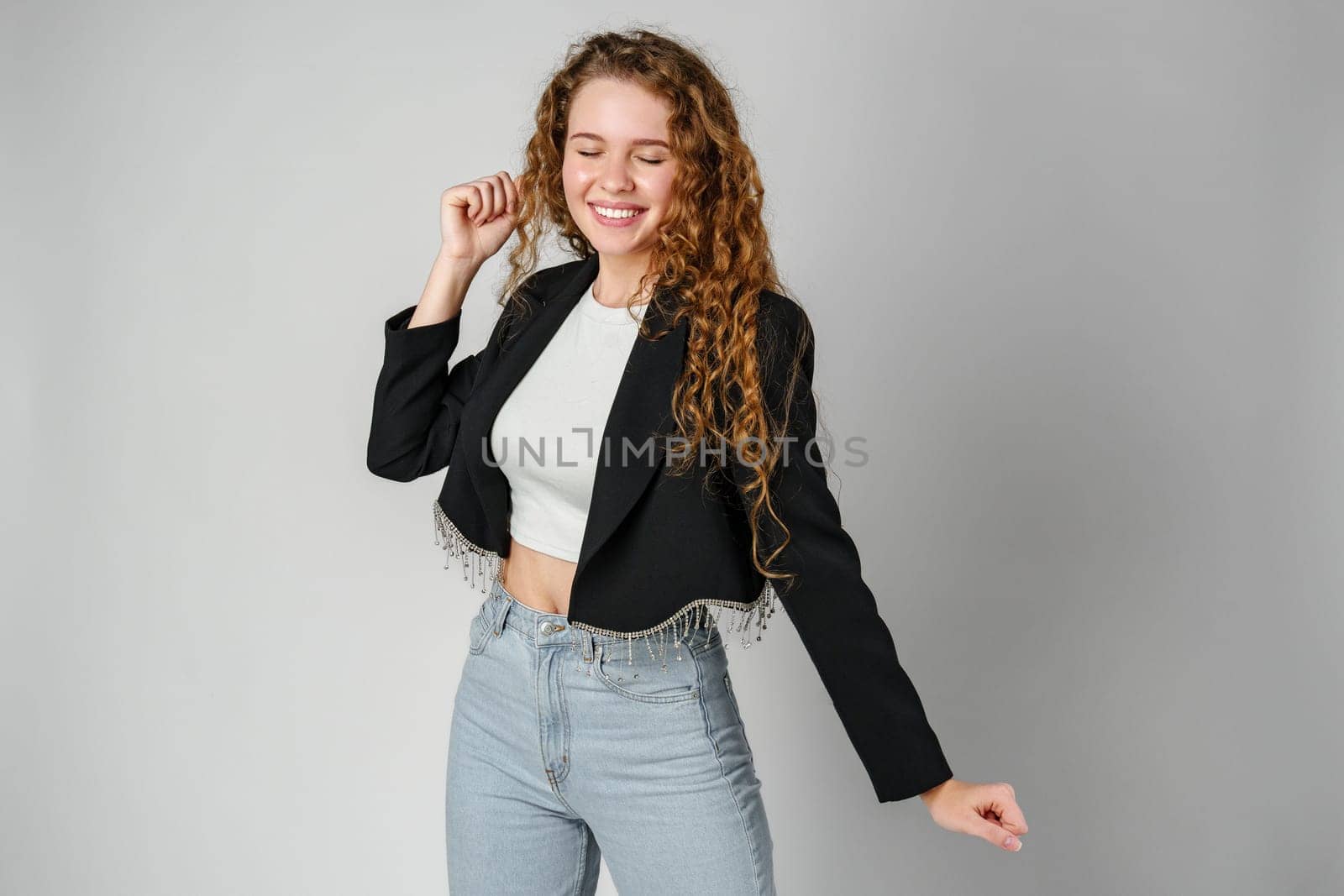 Joyful Young Woman Dancing Alone in Light-Colored Casual Attire Against a Grey Background by Fabrikasimf