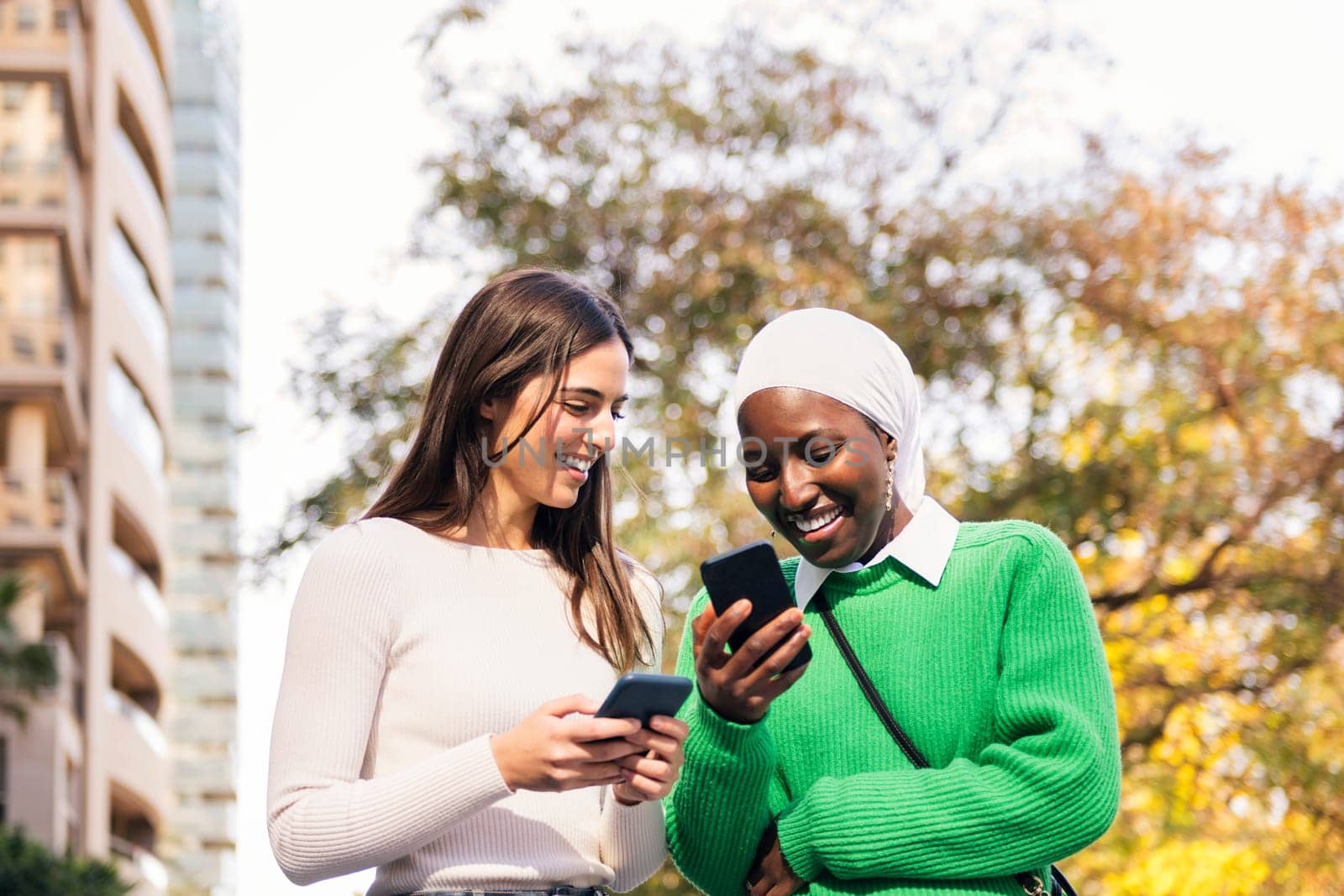 two young women smiling happy looking their mobile phones, concept of friendship and technology, copy space for text
