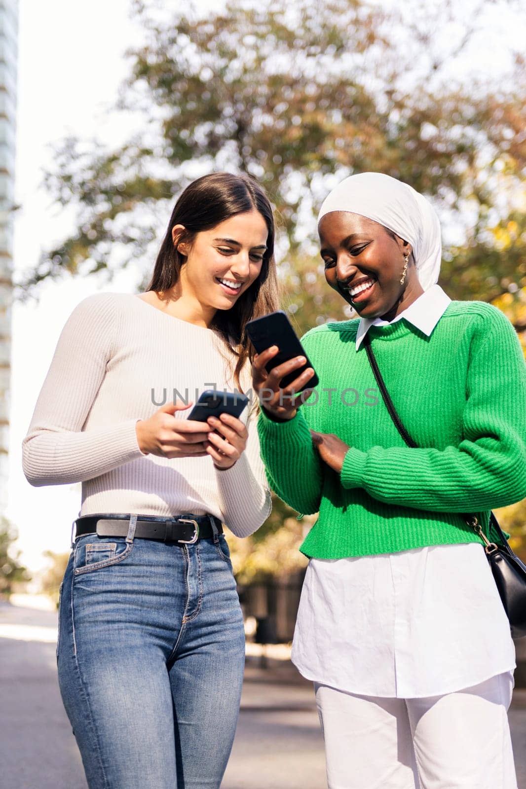 two young women smiling happy looking their mobile phones, concept of friendship and technology
