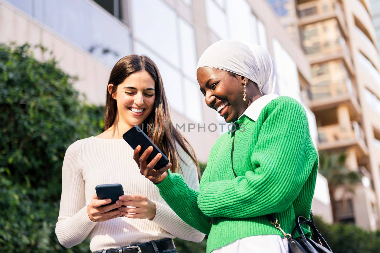 two young female friends smiling happy looking their mobile phones, concept of friendship and technology