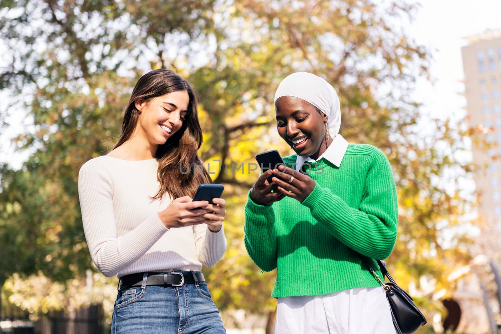 two young female friends smiling happy using their mobile phones, concept of friendship and technology