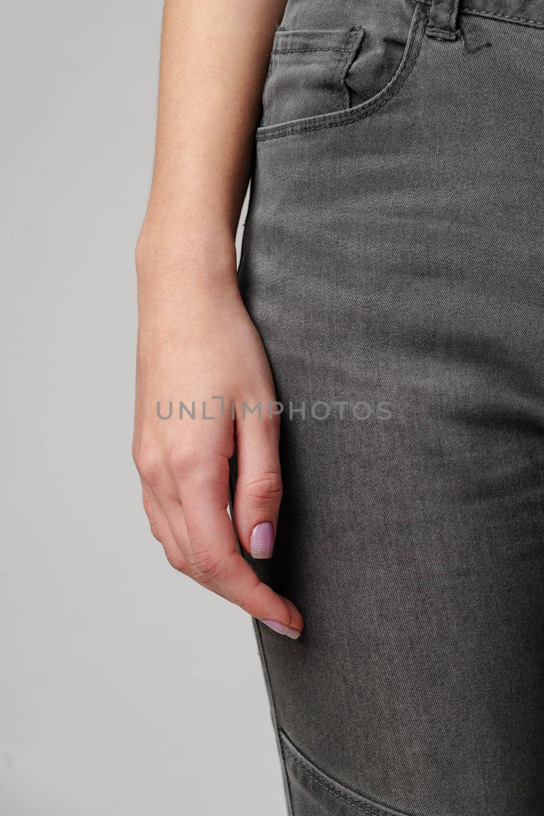 Close up of female hand on jeans in studio on gray background