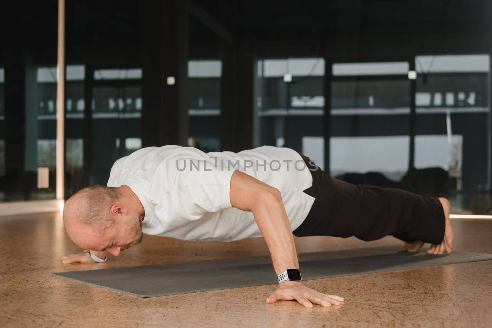 An athletic young man does exercises in the fitness room. A professional guy does yoga in the gym by Lobachad