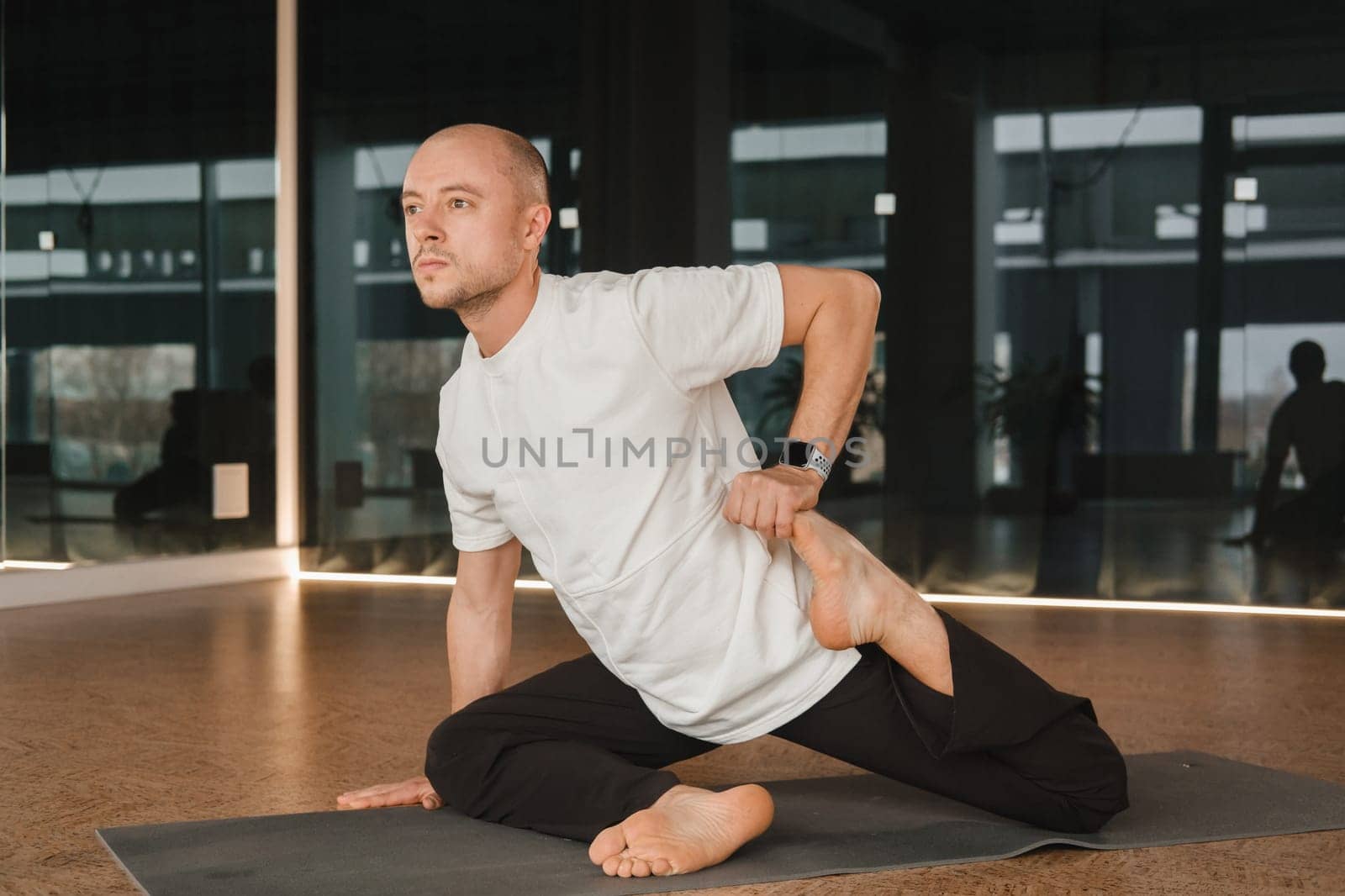 An athletic young man does exercises in the fitness room. A professional guy does yoga in the gym by Lobachad