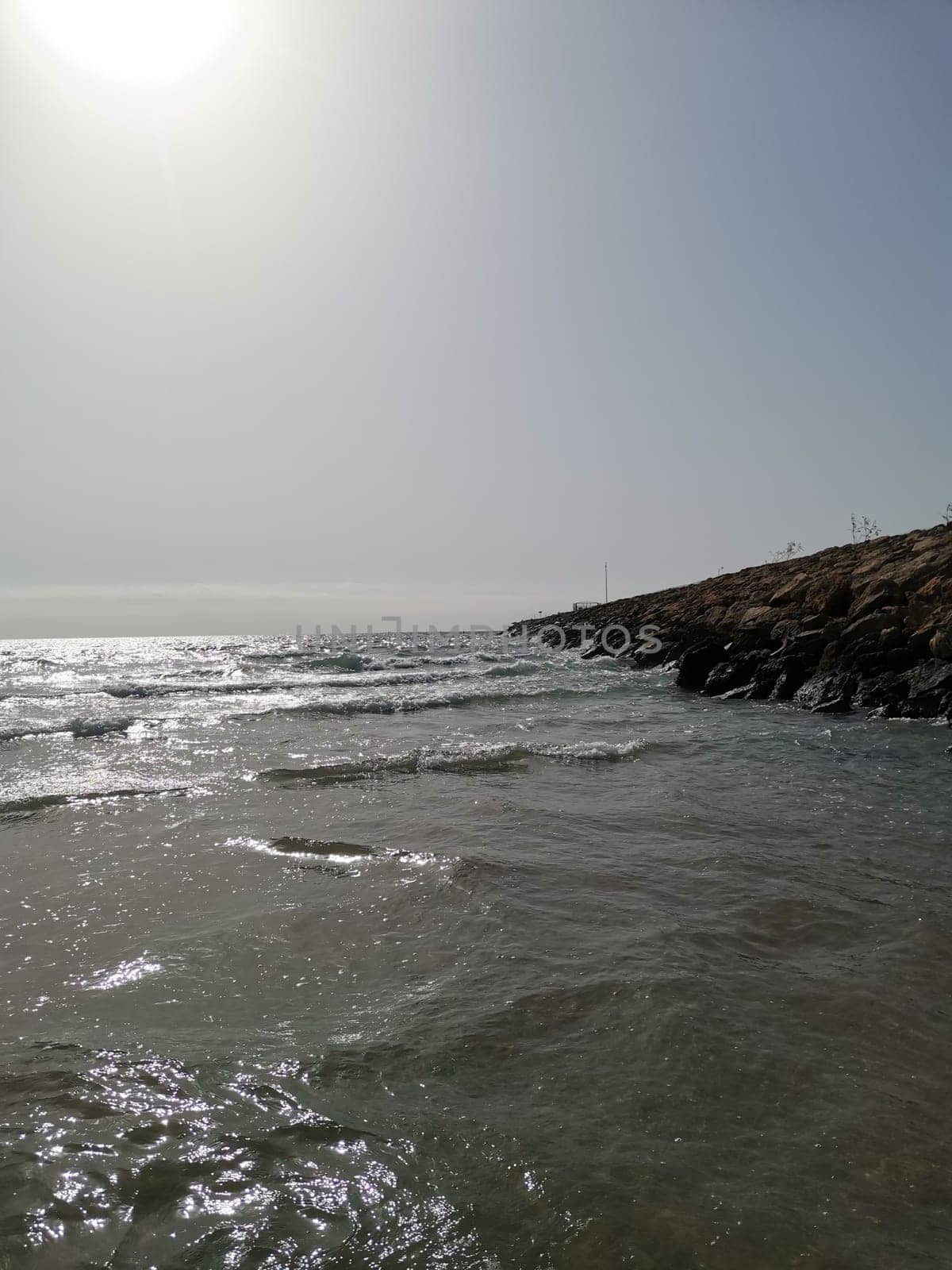 A vast expanse of liquid water with a rugged shore in the distance, under a clear sky. The landscape features coastal and oceanic landforms, with wind waves breaking on the shore