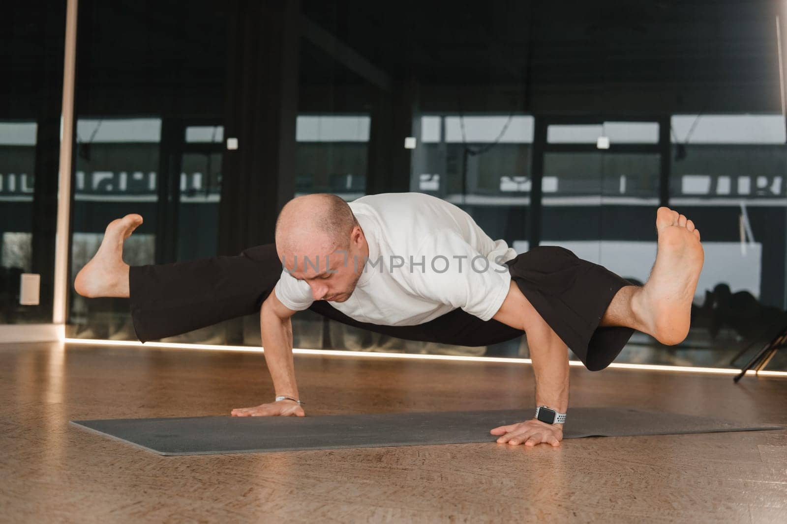 An athletic young man does exercises in the fitness room. A professional guy does yoga in the gym by Lobachad