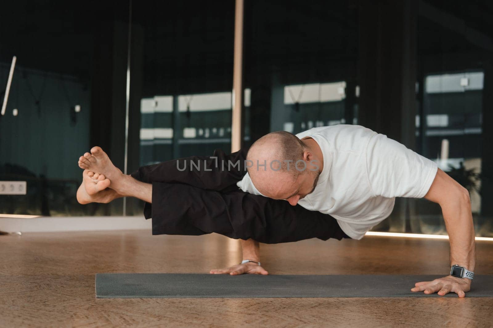 An athletic young man does exercises in the fitness room. A professional guy does yoga in the gym by Lobachad