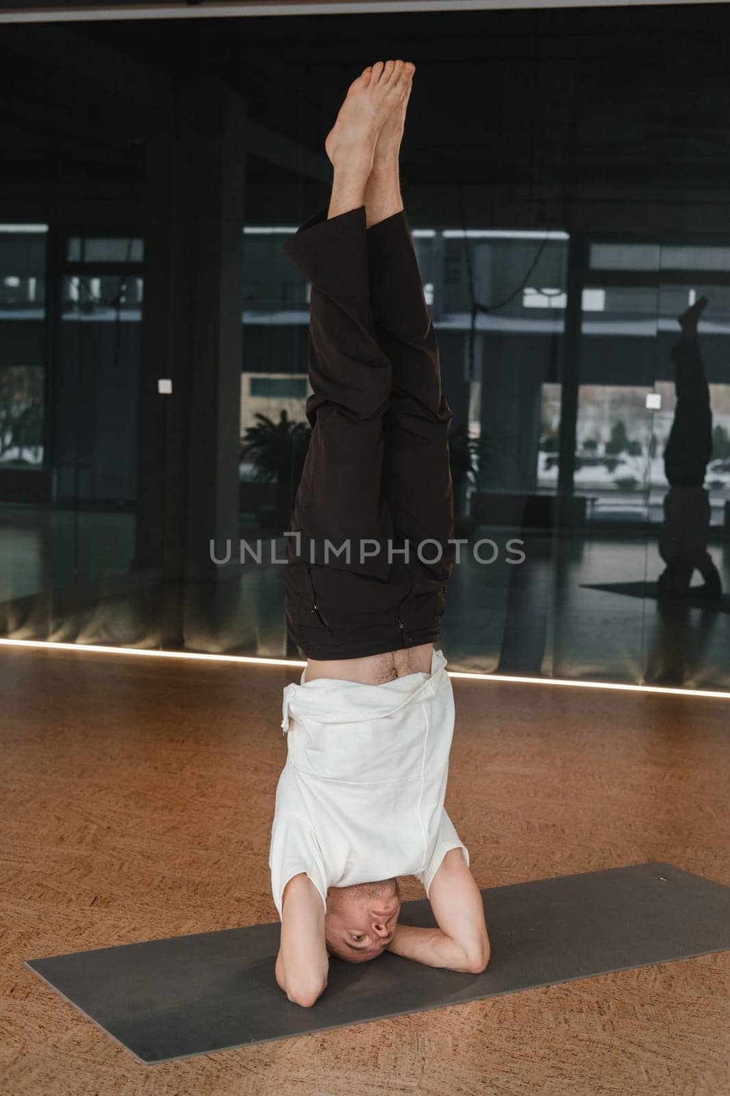 An athletic young man does exercises in the fitness room. A professional guy does yoga in the gym by Lobachad