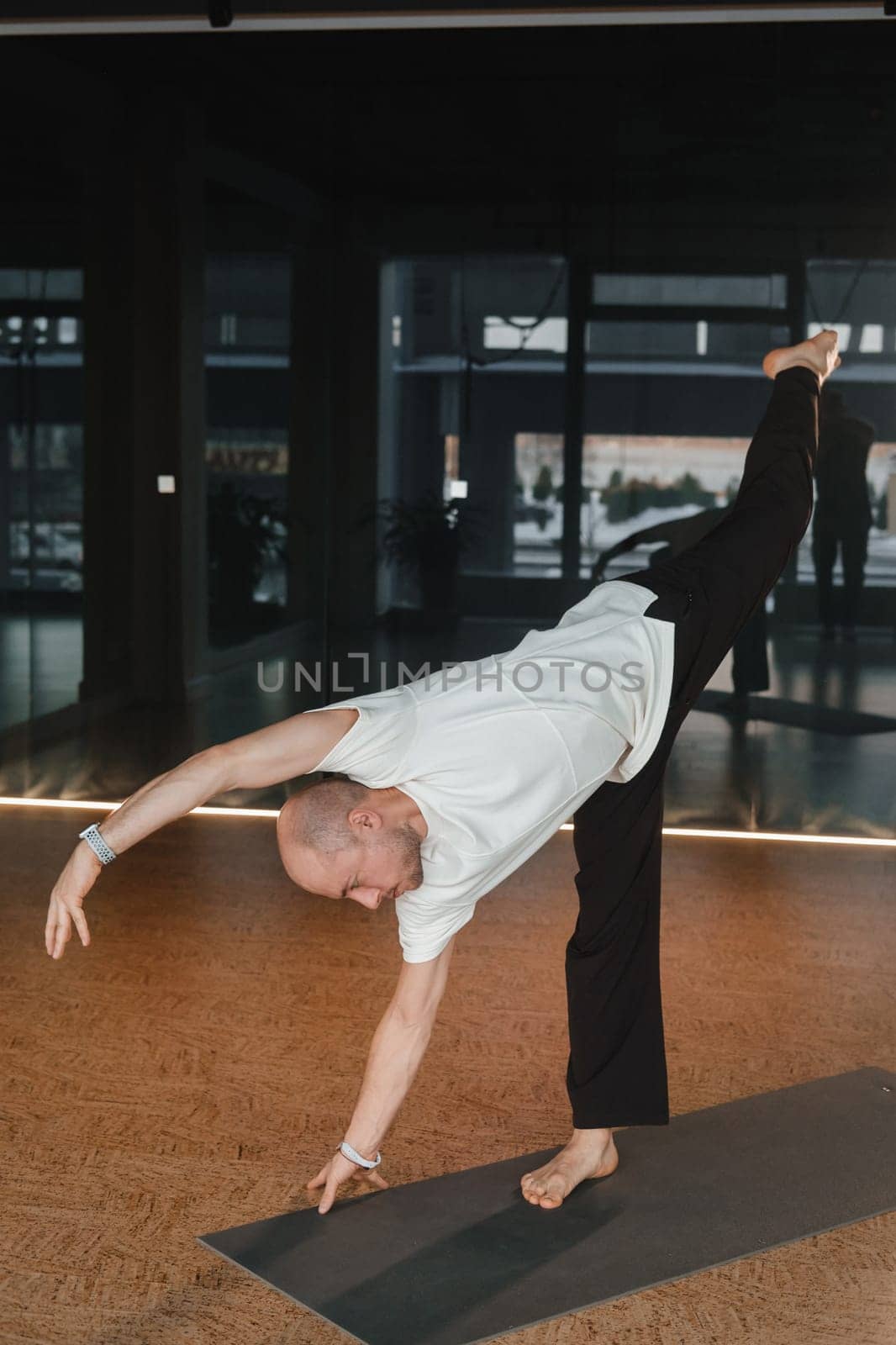 An athletic young man does exercises in the fitness room. A professional guy does yoga in the gym by Lobachad