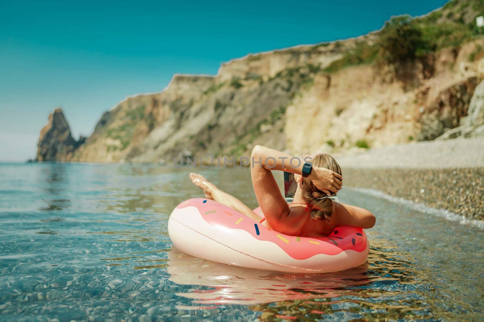 Woman laptop sea. Freelancer woman in sunglases floating on an inflatable big pink donut with a laptop in the sea. People summer vacation rest lifestyle concept by Matiunina